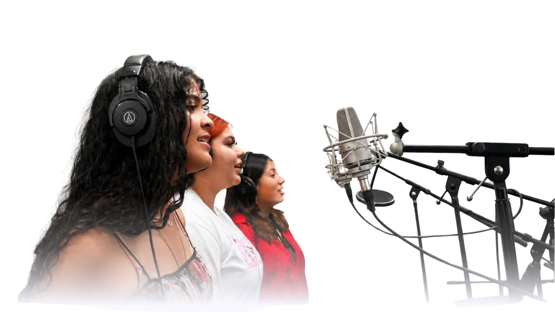 Three women wearing headphones sing into studio microphones during a music recording session.